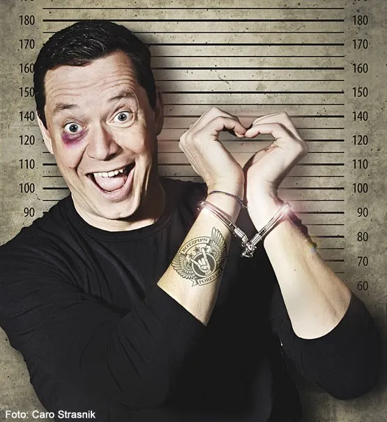 Mann lachend mit Handschellen um die Arme und Blau geschminktem Auge