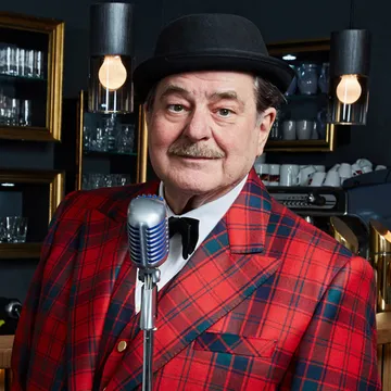 Erwin Steinhauer mit Hut und Fliege vor einem Mikrofon