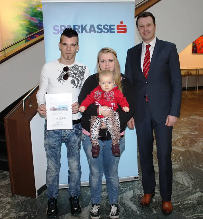 zwei Männer und eine Frau mit Kind in der Hand lachen in die Kamera
