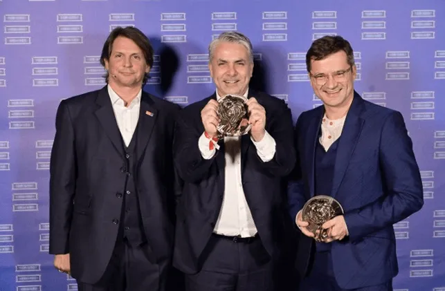 drei Männer davon halten zwei einen Award in die Kamera 