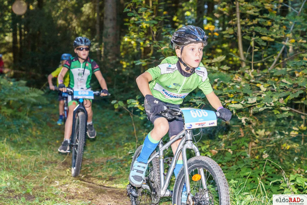 drei Kinder auf Rädern hintereinander im Wald