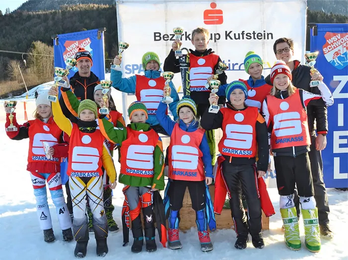 Kinder lachend im Skianzug mit Pokal in der Hand