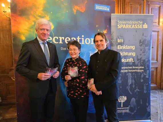 Zwei Männer in Anzügen flankieren die Chefdirigentin von recreation und halten das Programmheft in den Händen.