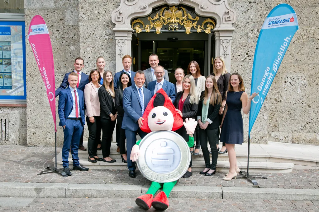 Sparkassenvorstände Christoph Paulweber und Markus Sattel (Bildmitte rechts und links) freuen sich gemeinsam mit dem Sparefroh über 14 neue Kolleginnen und Kollegen in der Salzburger Sparkasse