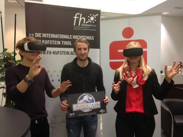 ein Mann und eine Frau mit virtueller Brille und ein Mann in der Mitte mit Jurassic World Plakat 