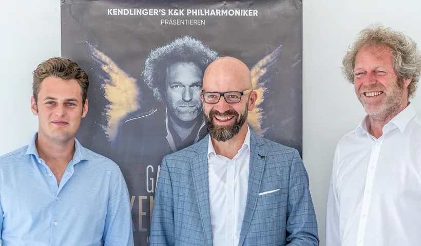 drei Herren vor einem Plakat lachen in die Kamera