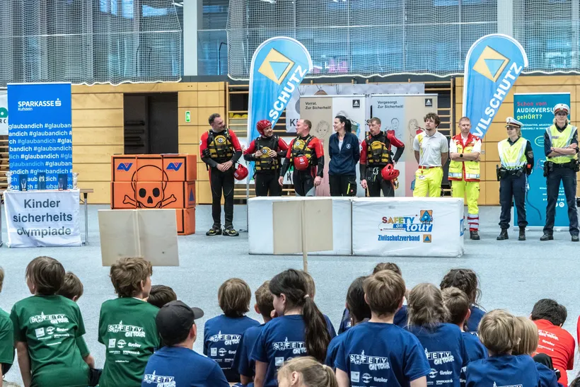 Kinder sitzen und blicken gespannt auf die Herren des Zivilschutzes