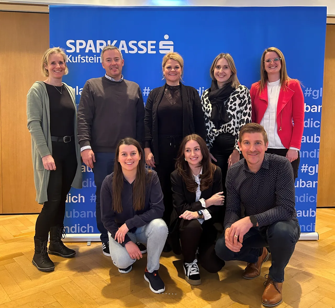 8 Personen stehen bzw. knien für ein Gruppenfoto vor einem Sparkasse Kufstein Aufsteller