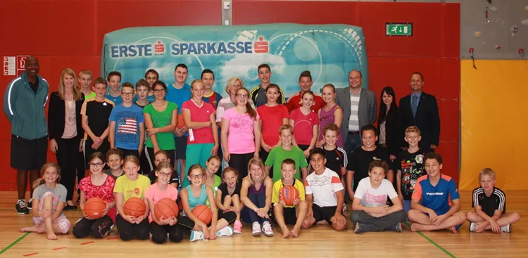 sitzende und stehende Kinder in einer Turnhalle mit Basketbälle in der Hand