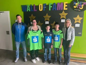 Zwei Damen, ein Herr und zwei Kinder mit Sparkassen-Trikots in einer Schule