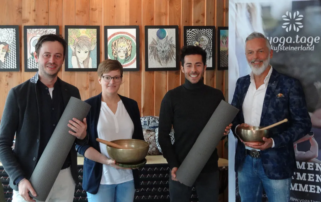 4 Personen halten Yoga-Matten und Klangschalten in den Händen und lächeln in die Kamera