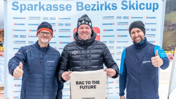 drei Herren mit Winterkleidung und Mützen vor dem Sparkasse Bezirks Skicup Aufsteller zeigen das Sackerl "Bag to the Future" und machen Daumen hoch