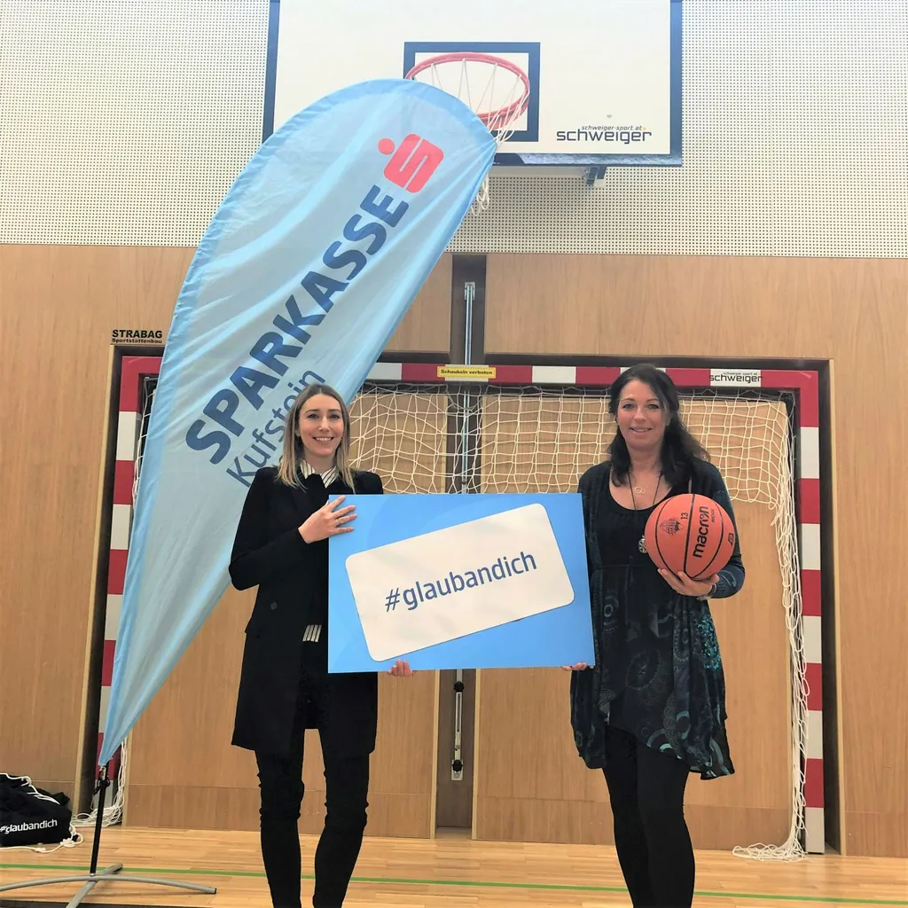 zwei Damen halten Basketball und #glaubandich Schild in Turnhalle