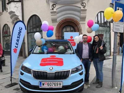 zwei Personen neben Sparkasse foliertem Auto