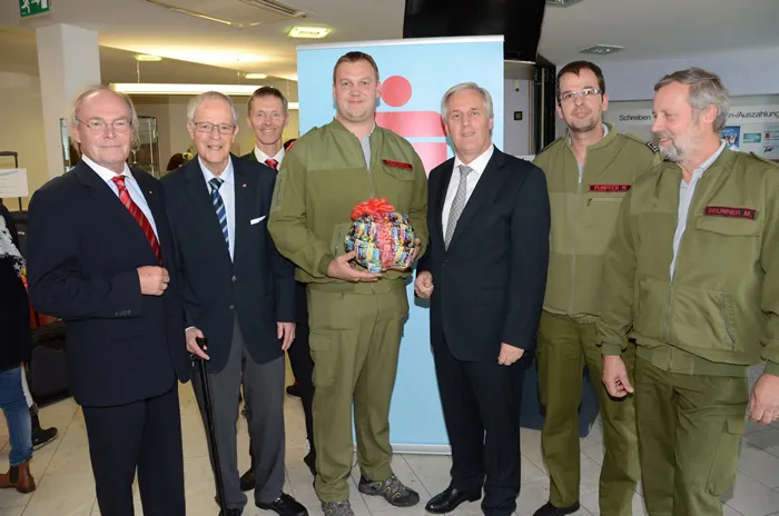 drei stehende Feuerwehrmänner und vier stehende Männer schauen lachend in die Kamera