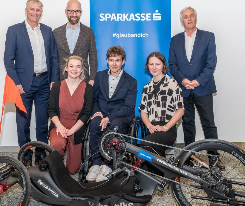 sechs Personen lächeln in die Kamera, im Vordergrund das Sportgerät