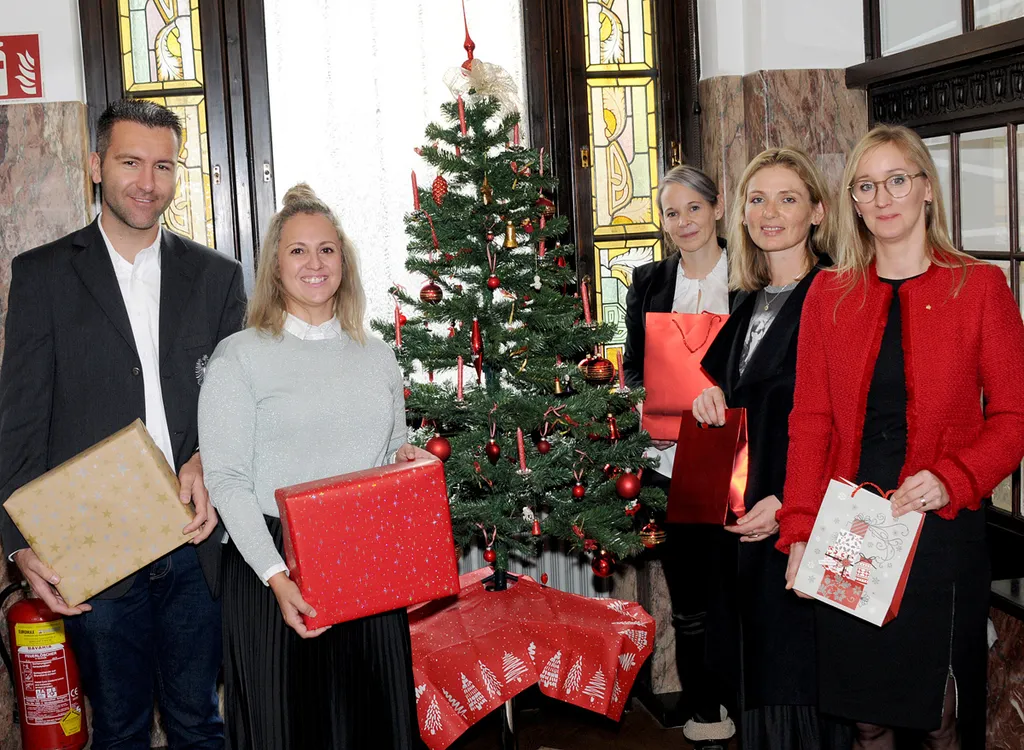 fünf Personen neben Christbaum und Geschenke in der Hand