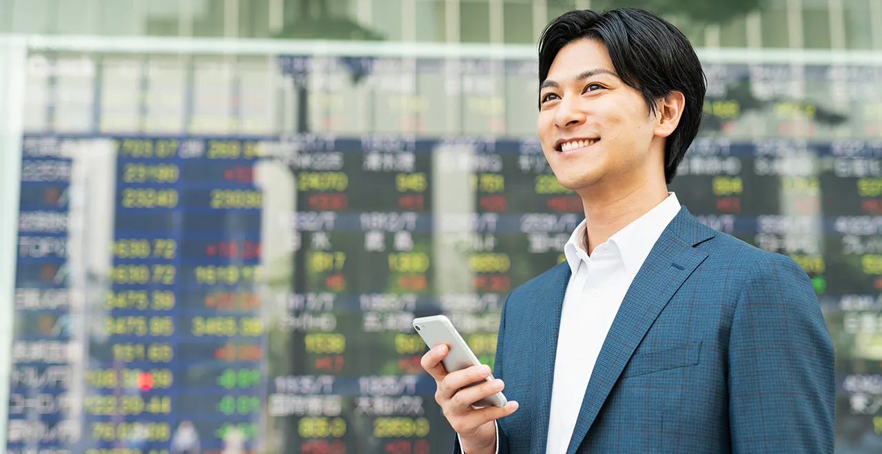 Junger asiatischer Businessmann vor Videowall mit Börsenkursen