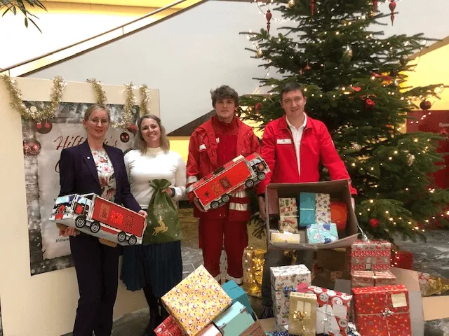 zwei Rettungsmänner und zwei Frauen mit Geschenken neben dem Christbaum 