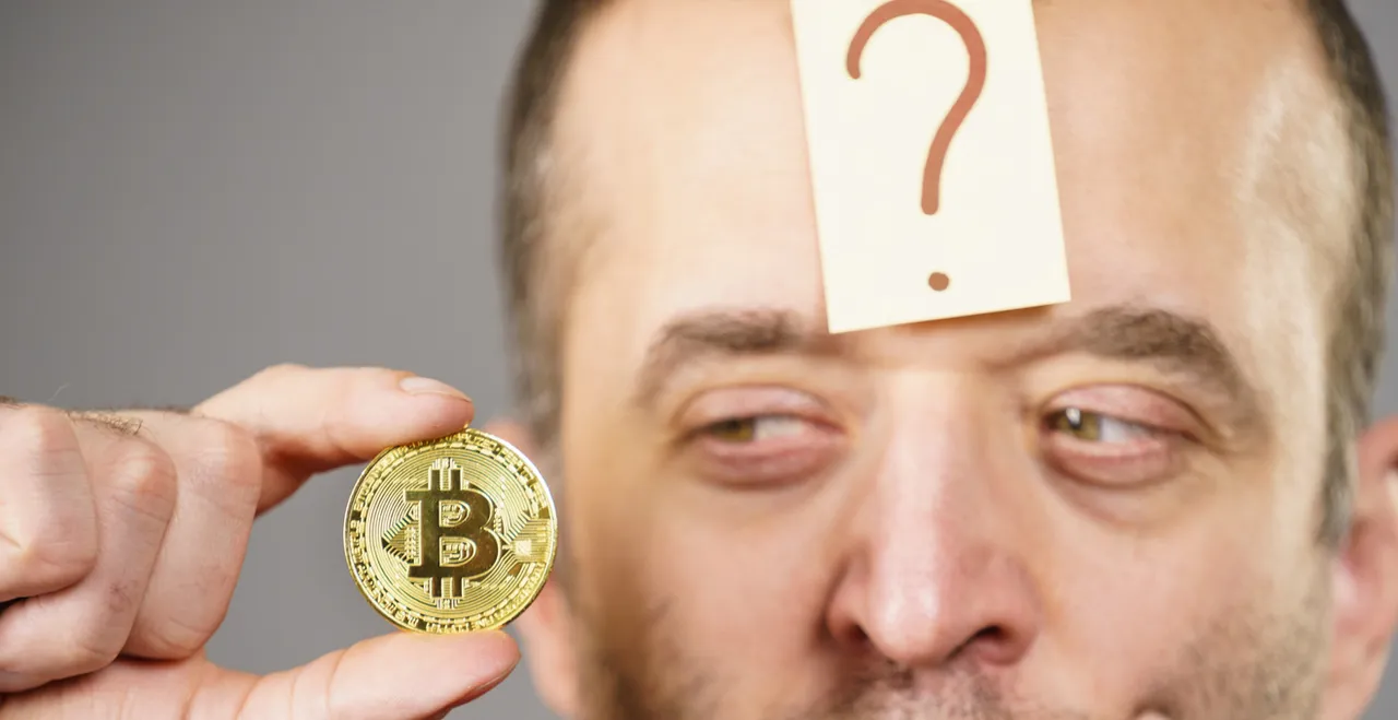 Mann mit Fragezeichen auf der Stirn betrachte eine Bitcoin-Münze