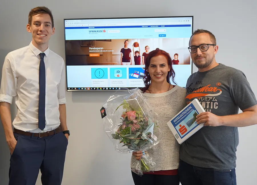 Kundenbetreuer Bernd Panholzer (links) übergibt den glücklichen Gewinnern Nathalie und Florian Schauer ihren Hochzeitsreise-Gutschein in der Sparkassen-Filiale Neunkirchen Bahnstraße.