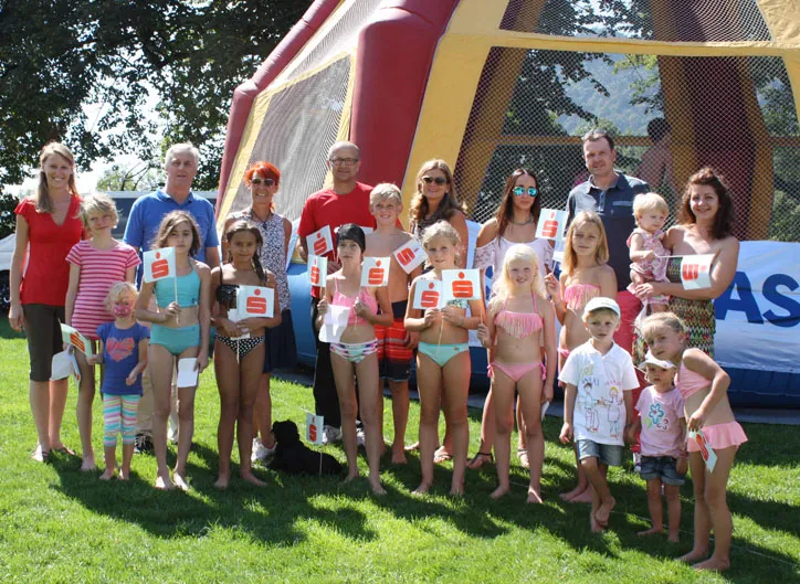 stehende Kinder im Badeanzug und Sparkasse Flagge in der Hand und stehende Personen im Hintergrund