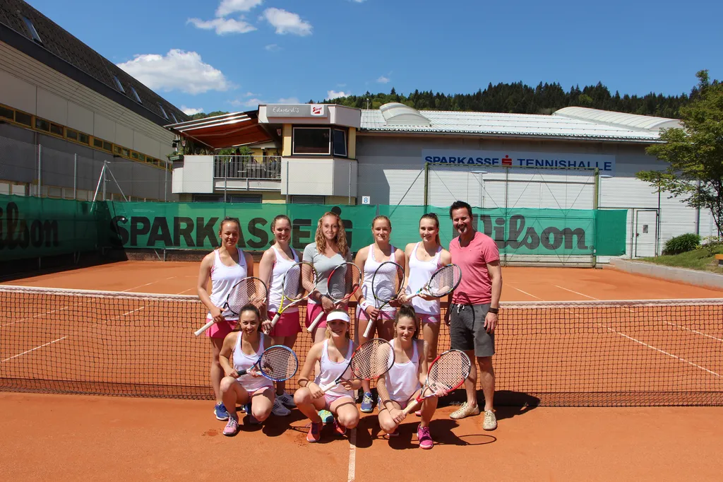 acht Frauen mit Tennisschläger in der Hand und ein Mann stehen vor Tennisnetz 