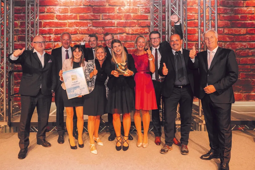 Gruppenfoto, Personen in schöner Kleidung halten Urkunde und machen Daumen Hoch