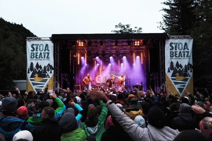 Menschenmenge vor einer mit Schweinwerfern beleuchteten Bühne auf der die Band gerade spielt